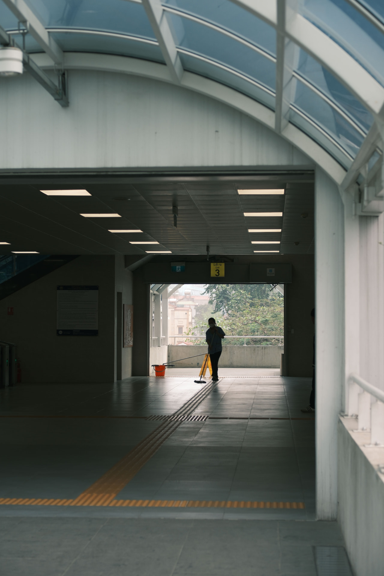 A custodian mopping a covered walkway beside a wet-floor sign