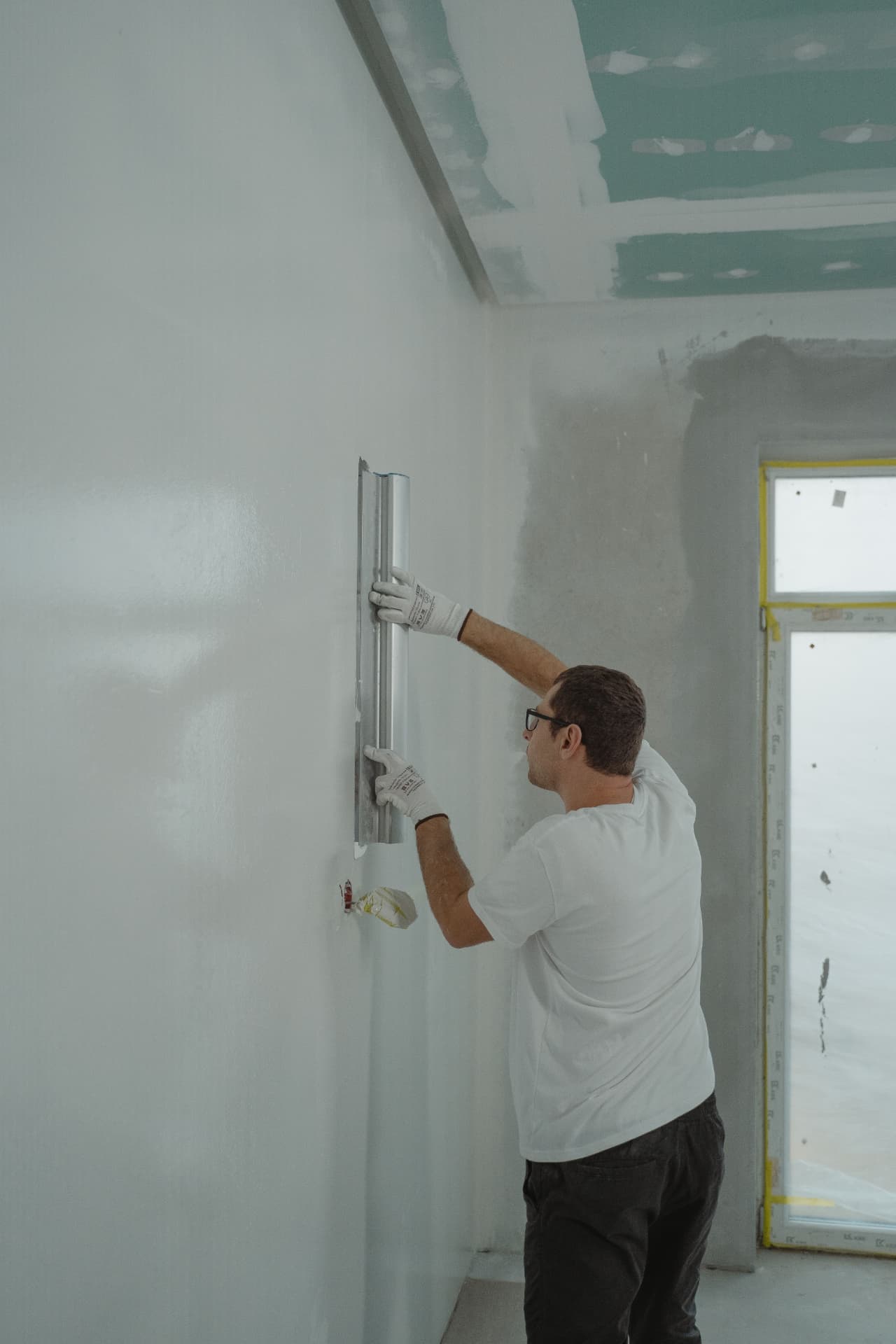 A contractor smoothing joint compound across a drywall wall with a wide taping blade