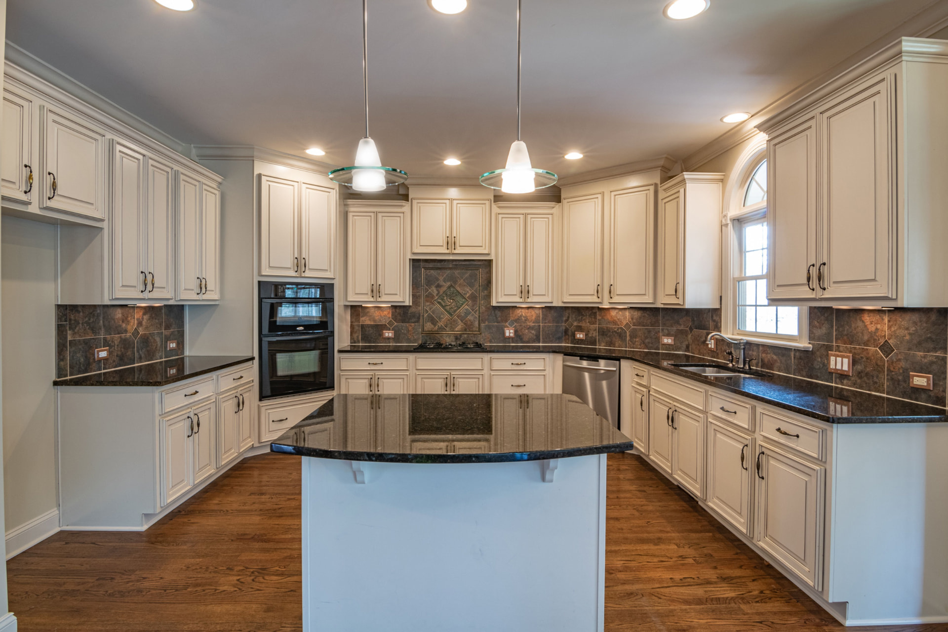 A finished residential kitchen with off-white cabinets, dark stone countertops and a central island