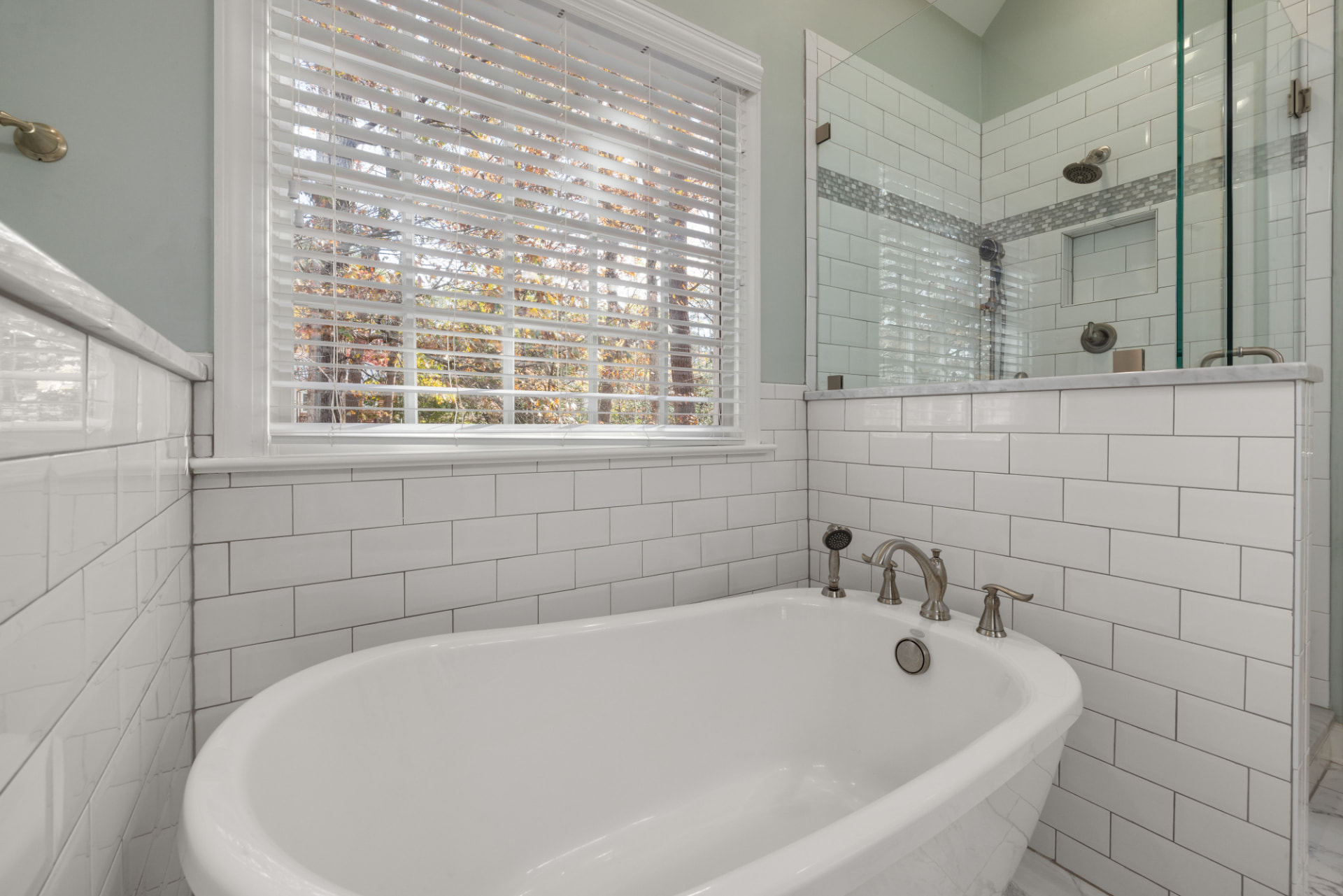 A bright bathroom with a freestanding white bathtub, subway-tiled walls and a glass-enclosed shower