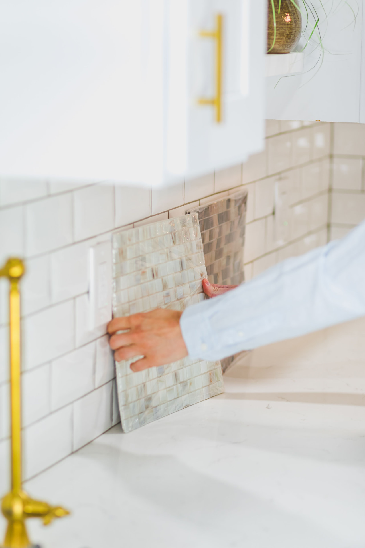 A designer holding a mosaic tile sample against a kitchen backsplash